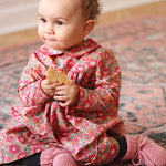 Baby girl wearing Lalaby Anna baby dress in Berry besty pink liberty organic cotton